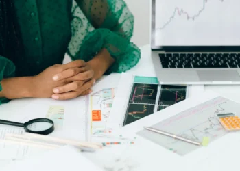 Hands folded next to printed charts, a magnifying glass, calculator and laptop displaying graphs illustrating ModularDS vs GoDaddy Pro Sites: Which Will Boost Your Workflow?